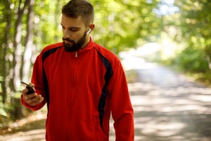 young athletic man with bluetooth headphones using mobile phone while jogging in forest