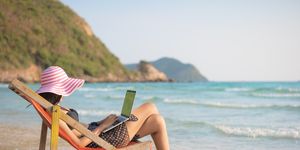 mujer con traje de baño y sombrero trabajando con un portátil en la playa