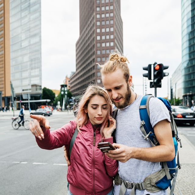 A Young Backpacking Couple Standing On Corner Of Busy City Street