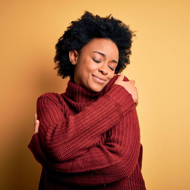 young beautiful african american afro woman with curly hair wearing casual turtleneck sweater hugging oneself happy and positive, smiling confident self love and self care