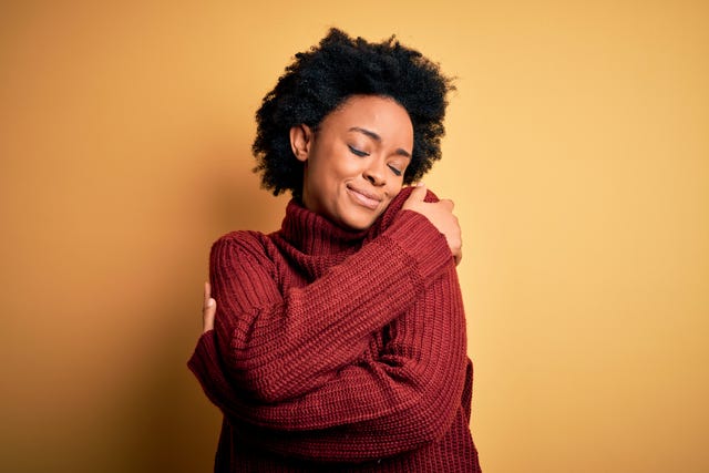 young beautiful african american afro woman with curly hair wearing casual turtleneck sweater hugging oneself happy and positive, smiling confident self love and self care