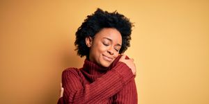 young beautiful african american afro woman with curly hair wearing casual turtleneck sweater hugging oneself happy and positive, smiling confident self love and self care