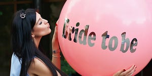 Young beautiful brunette bride to be with dark hair and silver crown on it kissing her pink bachelorette party balloon