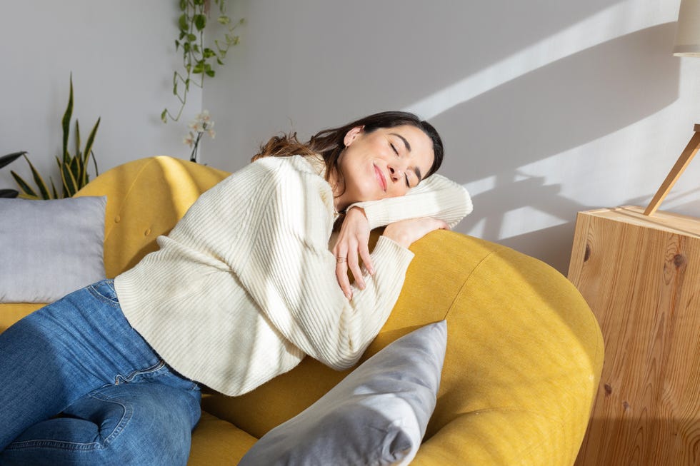 young beautiful woman enjoying sunlight resting on sofa at home simple living concept