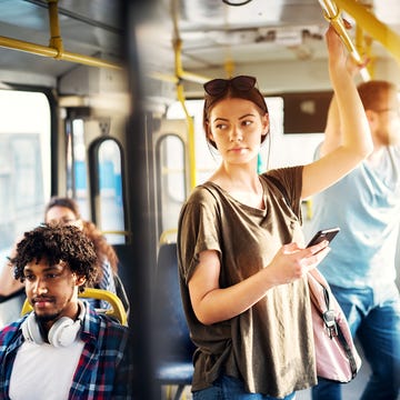 Young beautiful woman is standing in the bus using phone and holding onto the bar while waiting to arrive at her destination. Young beautiful woman is standing in the bus using phone and holding onto the bar while waiting to arrive at her destination.