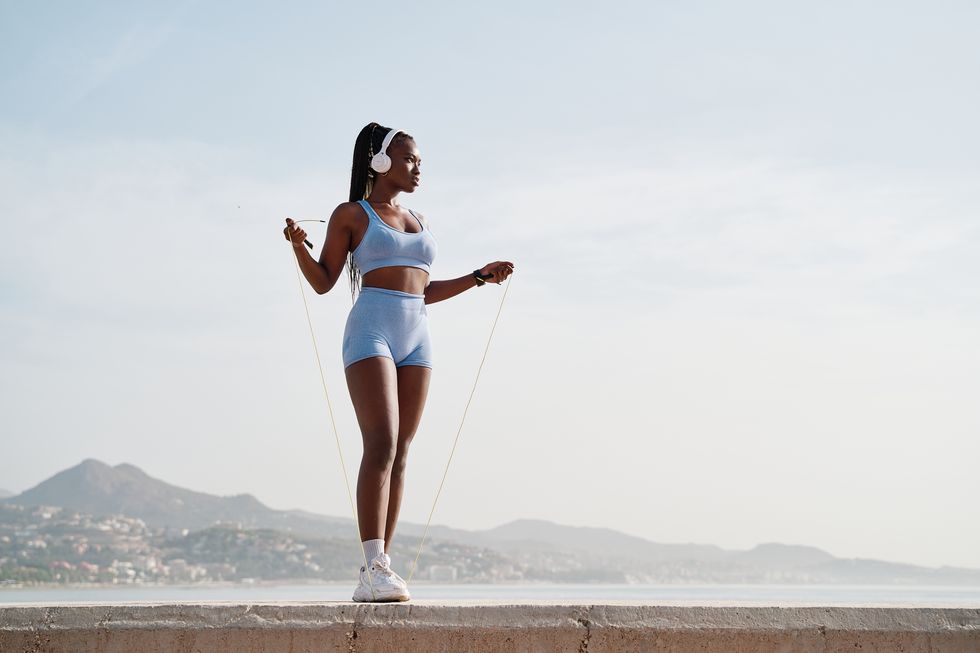 young black female athlete jumping rope on a stone wall near the sea