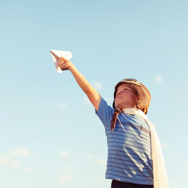 young boy dressed as pilot flies paper airplane