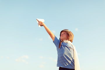 young boy dressed as pilot flies paper airplane