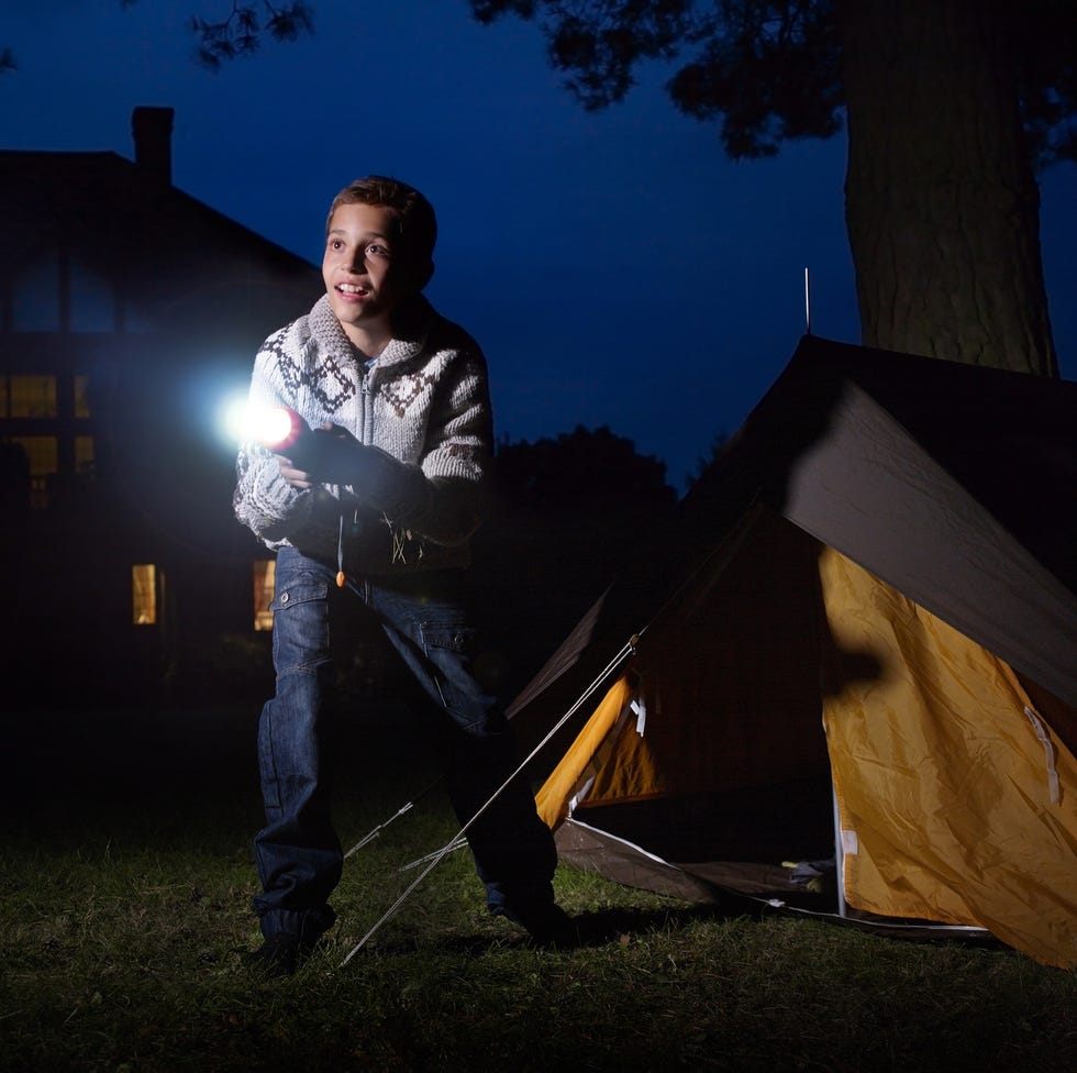 young boy outside tent shining torch into distance