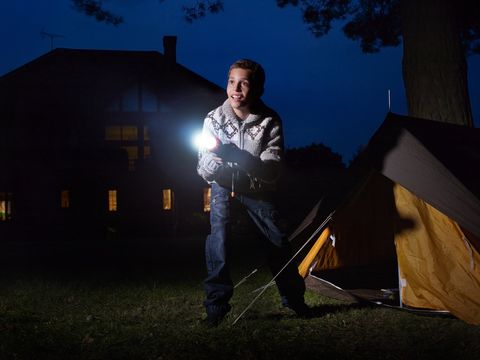young boy outside tent shining torch into distance