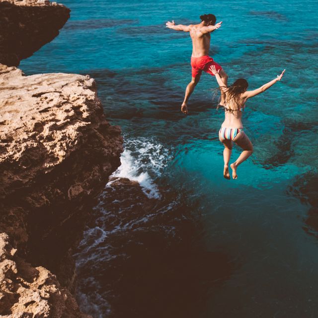 young brave divers couple jumping off cliff into ocean