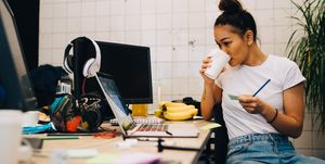 Young businesswoman drinking coffee while sitting at desk in small creative office