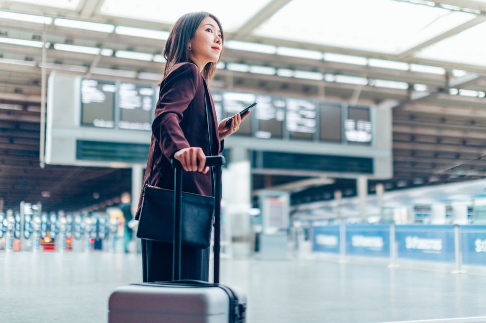 young businesswoman holding phone and carrying suitcase in airport