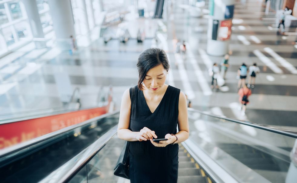 young businesswoman reading emails on smartphone while riding on escalator