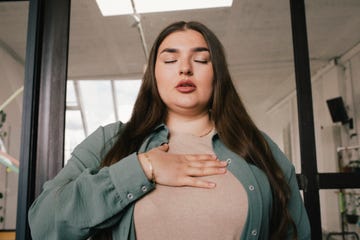 young businesswoman with eyes closed and hand on chest at office