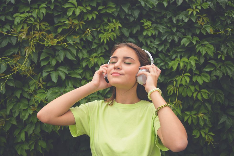 young caucasian brunette girl with headphones outdoors on sunny summer day
