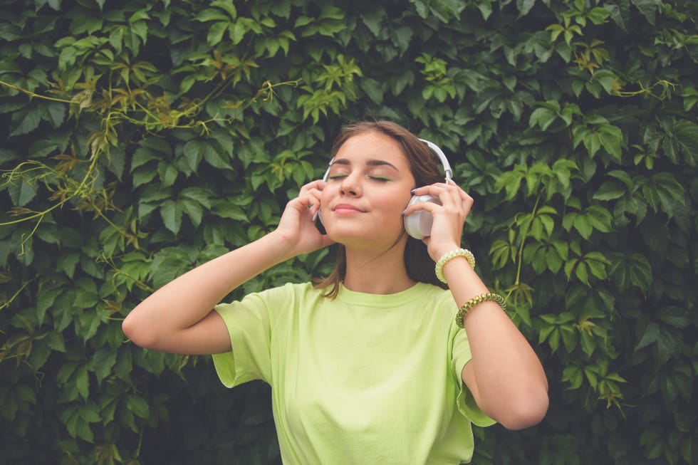 young caucasian brunette girl with headphones outdoors on sunny summer day