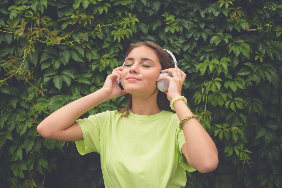 young caucasian brunette girl with headphones outdoors on sunny summer day