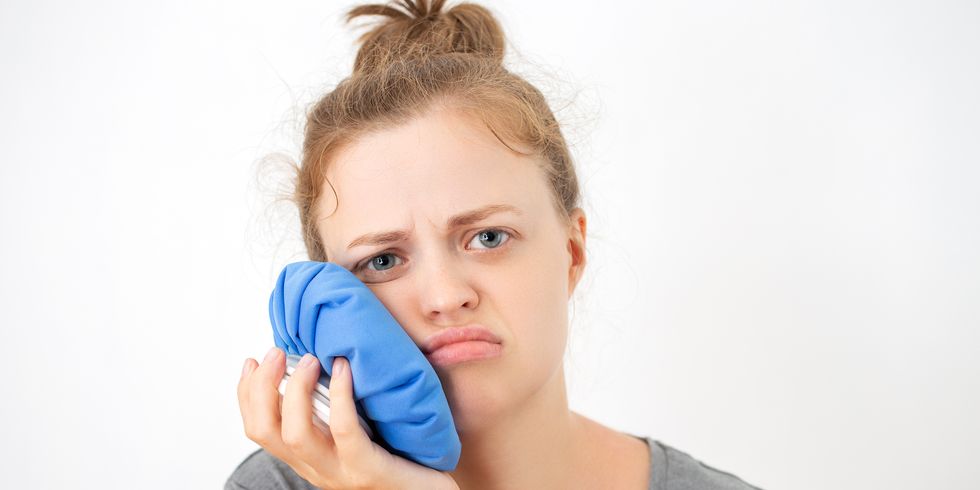 young caucasian woman holds ice bag to her cheek, suffering from a toothache or dental surgery
