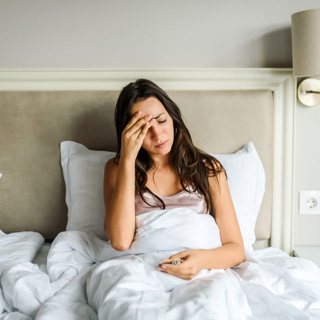 young lying in bed, feeling unwell, with her hand on her head sickness illness concept coronavirus fever headache concept home isolation