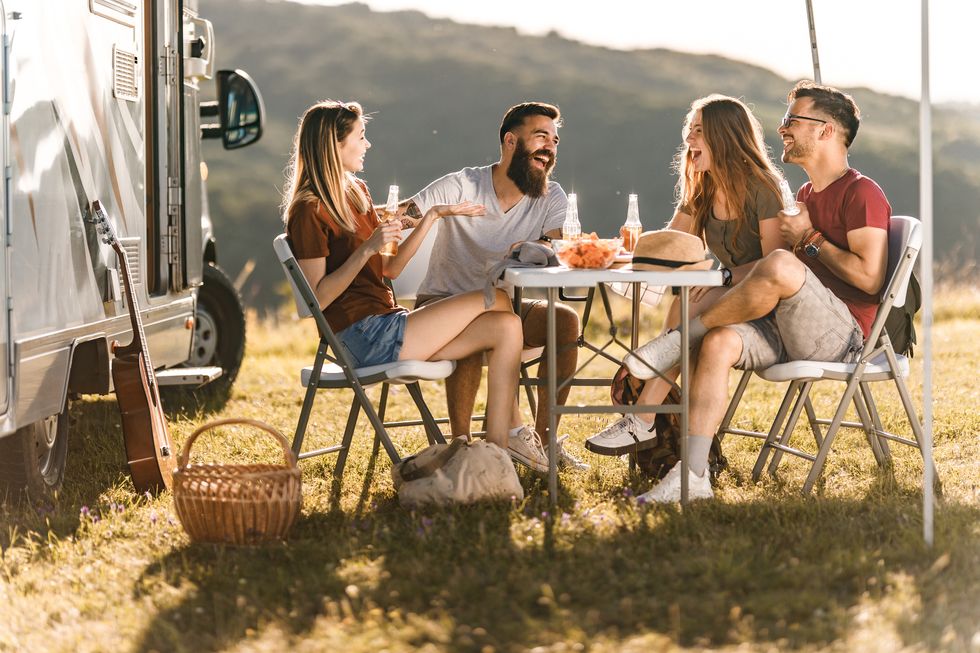 young cheerful couples talking at picnic table by the camp trailer
