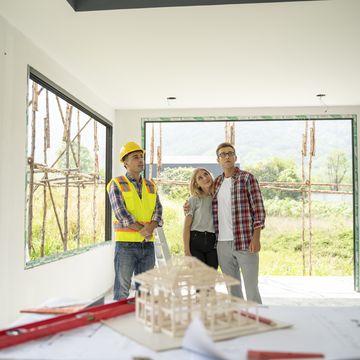 young couple and their agent examining blueprints at construction site.