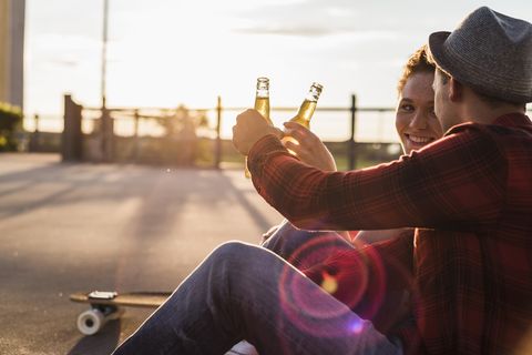 young couple clinking beer bottles at sunset
