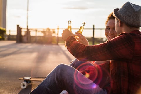 young couple clinking beer bottles at sunset