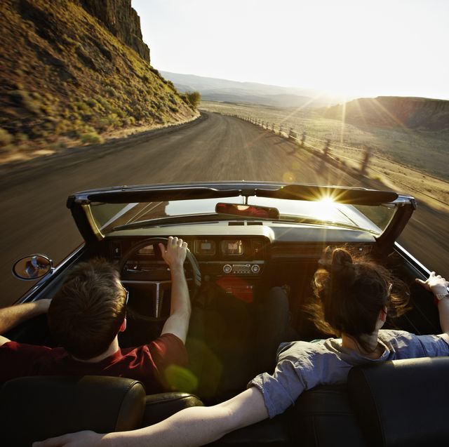 young couple driving convertible at sunset