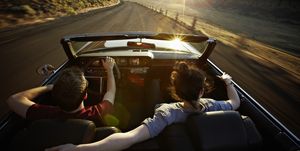 young couple driving convertible at sunset