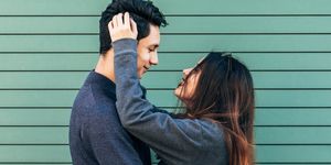 young couple embrace and look into each other's eyes while smiling, green background, valentine's day, young love