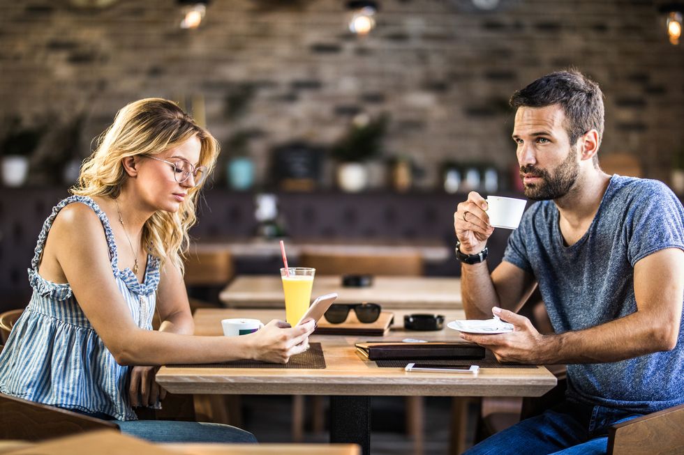 young couple ignoring each other while sitting in a cafe