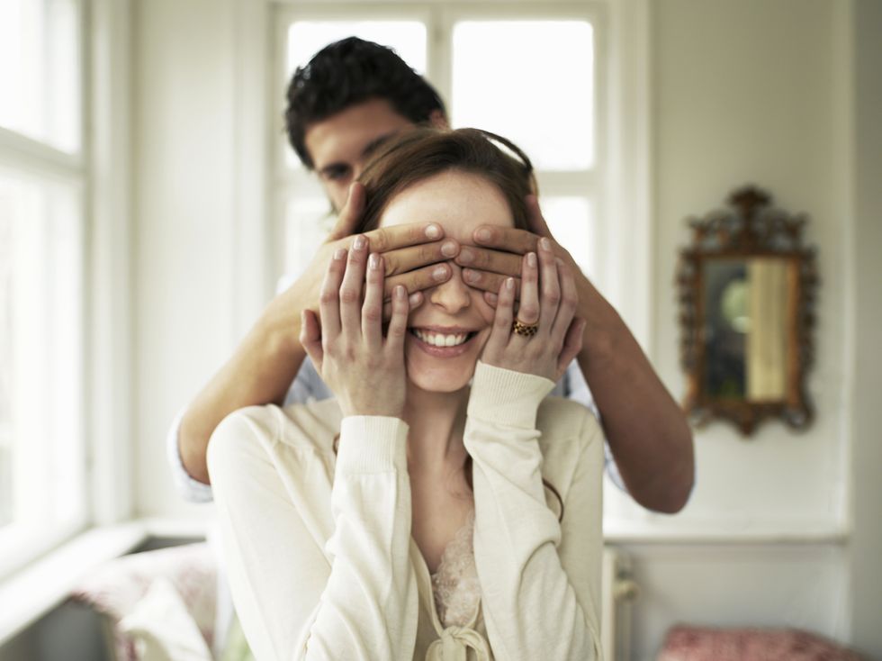 Young couple indoors, man covering woman's eyes