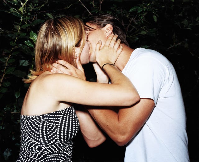 Young couple kissing near bush at night, side view