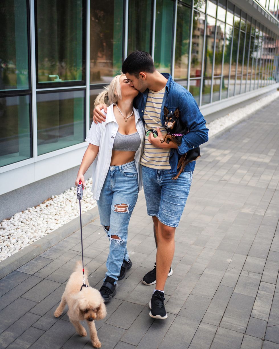 young couple kissing while taking their dogs for a walk