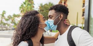 young couple kissing while wearing face surgical mask during coronavirus outbreak relationship and covid 19 concept image