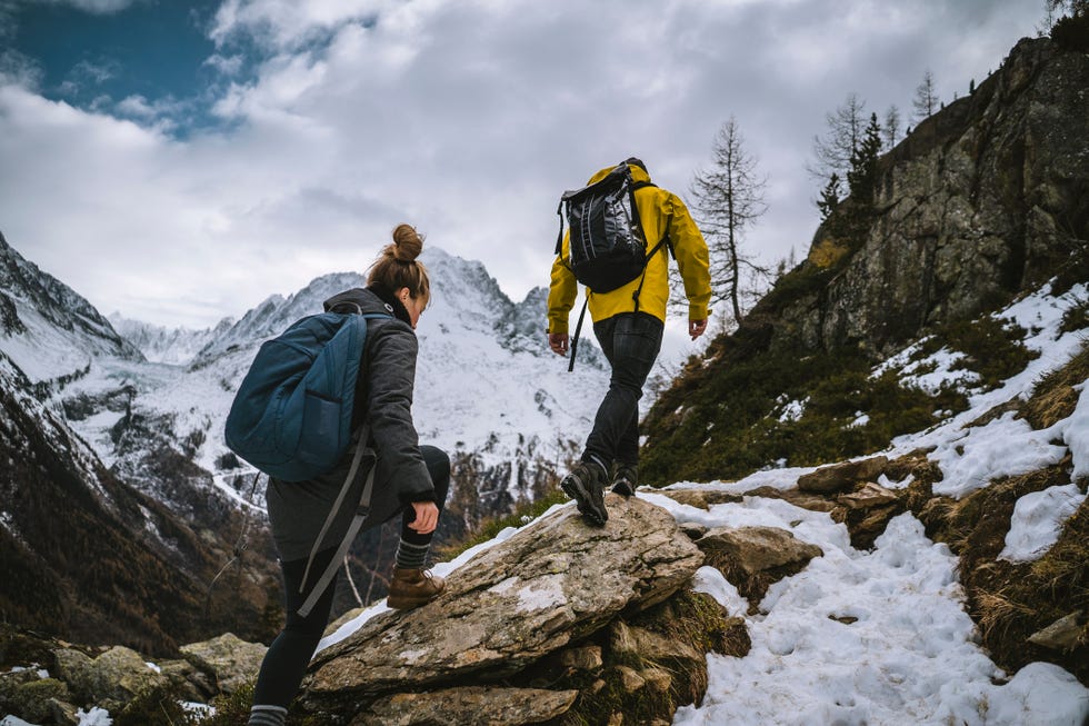 young couple of backpackers hike along a snowy ridge in the mountains