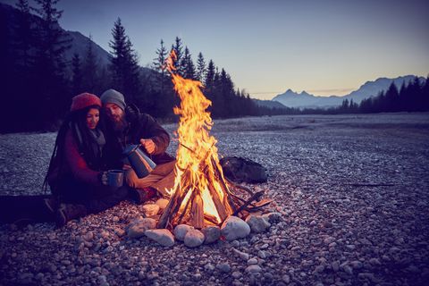 fun summer date ideas young couple pouring coffee by campfire at river isar, karwendel mountains, bavaria, germany