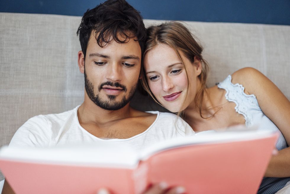 young couple reading book while sitting on bed at home