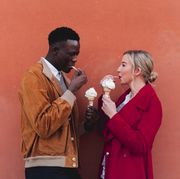 young couple standing at an orange wall eating ice cream