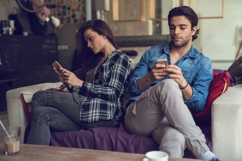Young couple text messaging on cell phones and ignoring each other.