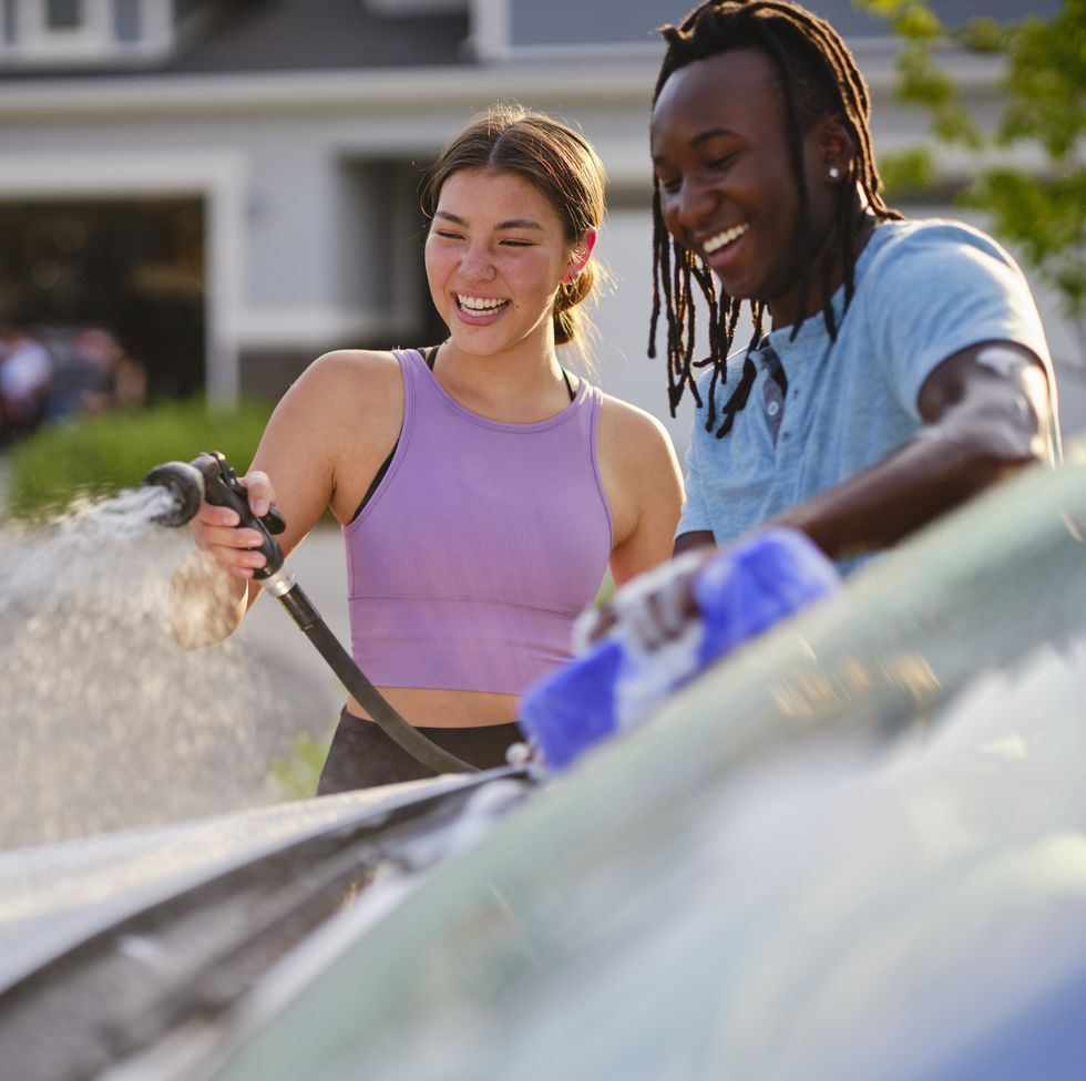 young couple washing a car in a driveway on a summer date