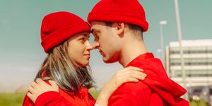 young couple wearing red overalls and hats standing head to head looking at each other