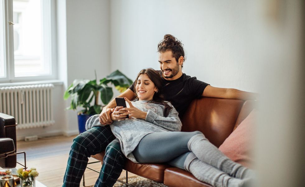 Young couple with mobile phone relaxing on sofa