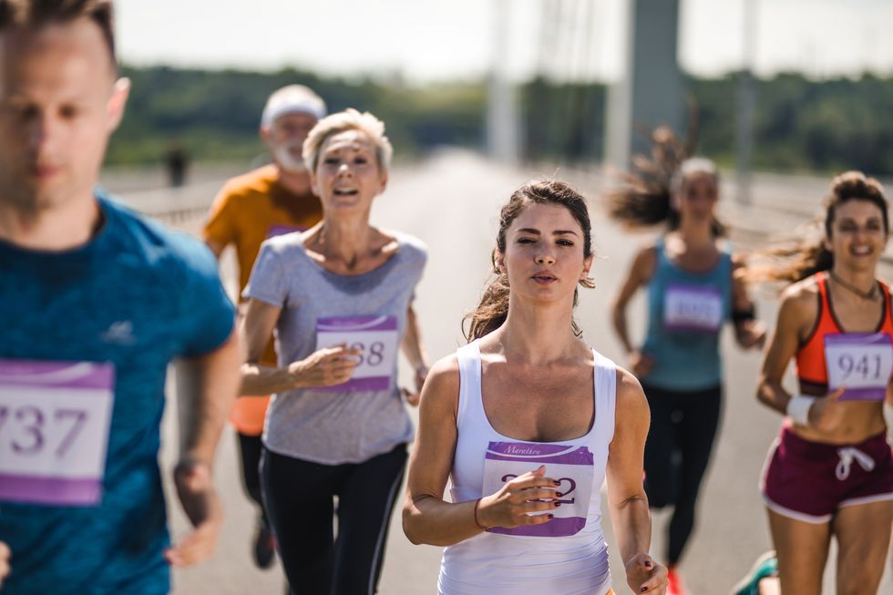 young determined woman running a marathon race with other competitors on the road