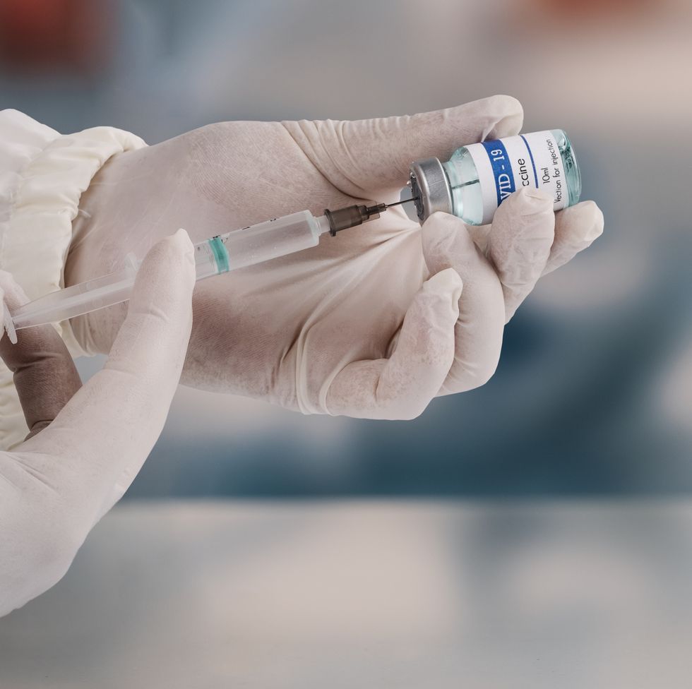 a young doctor in white protective glove is holding a medical syringe and vial