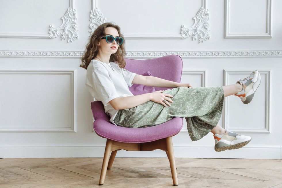 young fashionable woman model posing sitting on an armchair in the studio in trendy modern clothes from the new collection catalog