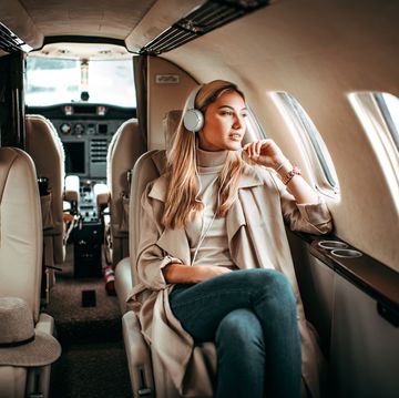young fashionable woman sitting on a private airplane and listening to music through headphones
