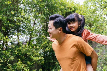 young father giving his daughter a piggyback ride and smiling in an outdoor park