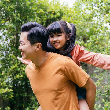 young father giving his daughter a piggyback ride and smiling in an outdoor park